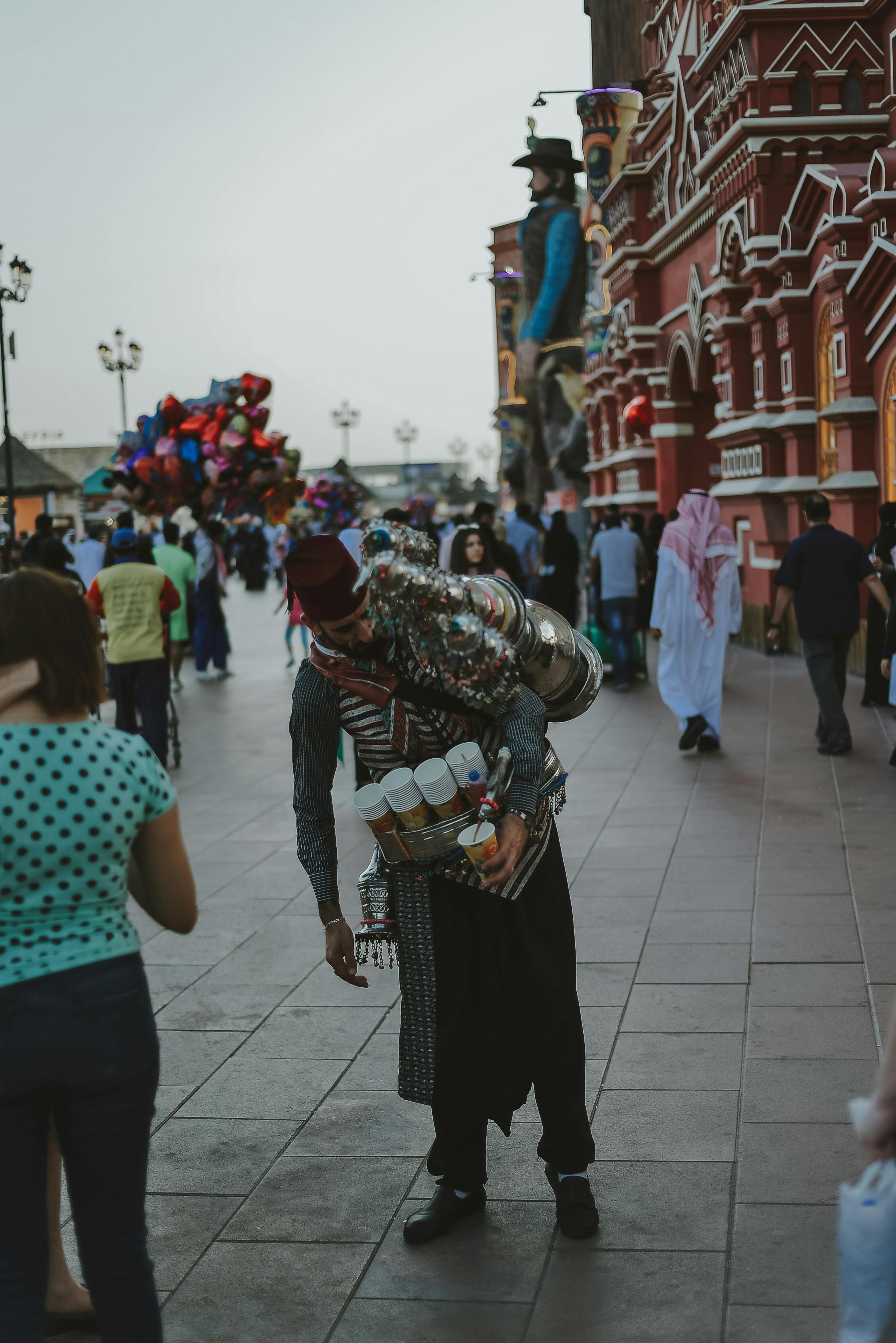 Traditional tea seller amidst a lively street scene in Dubai showcasing cultural attire and vibrant urban atmosphere.
