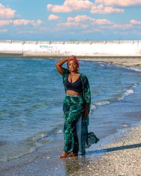 Confident woman in vibrant summer attire strolling along a sandy beach with blue skies and gentle waves.