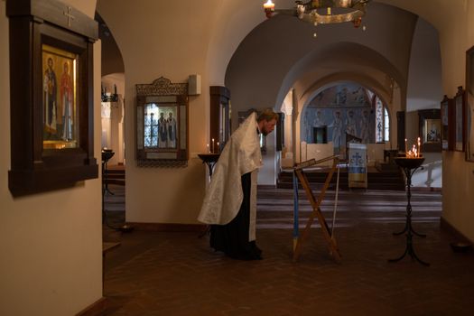 An Orthodox priest in vestments performs religious rituals inside a beautifully adorned church interior.