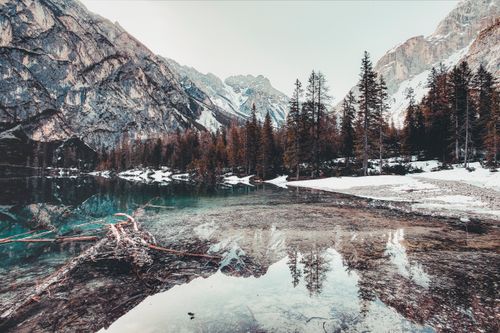 Free A tranquil winter scene of a clear lake surrounded by snowy mountains and pine trees. Stock Photo