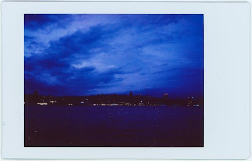 A Polaroid Picture of City Buildings  Near the Ocean Under Cloudy Sky 