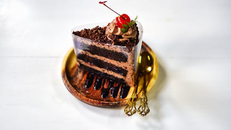 A Slice Of Chocolate Cake With Cherry On Top On A Wooden Saucer