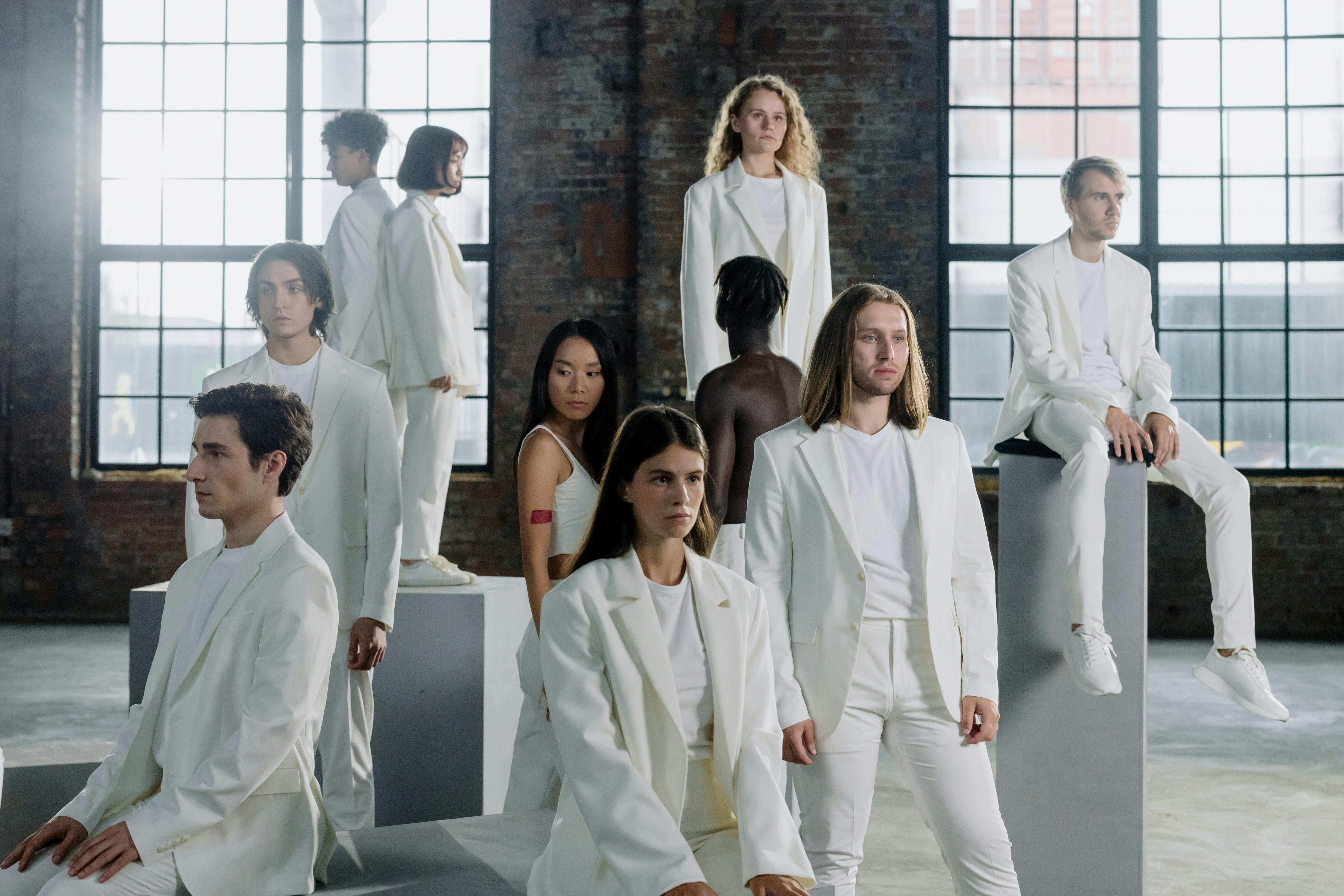 group of people in white suits standing in the room with brown brick walls and big windows