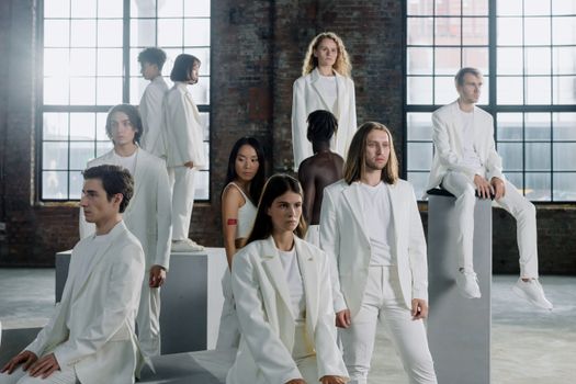 A diverse group of models wearing white suits in an industrial space, embodying unity and fashion.
