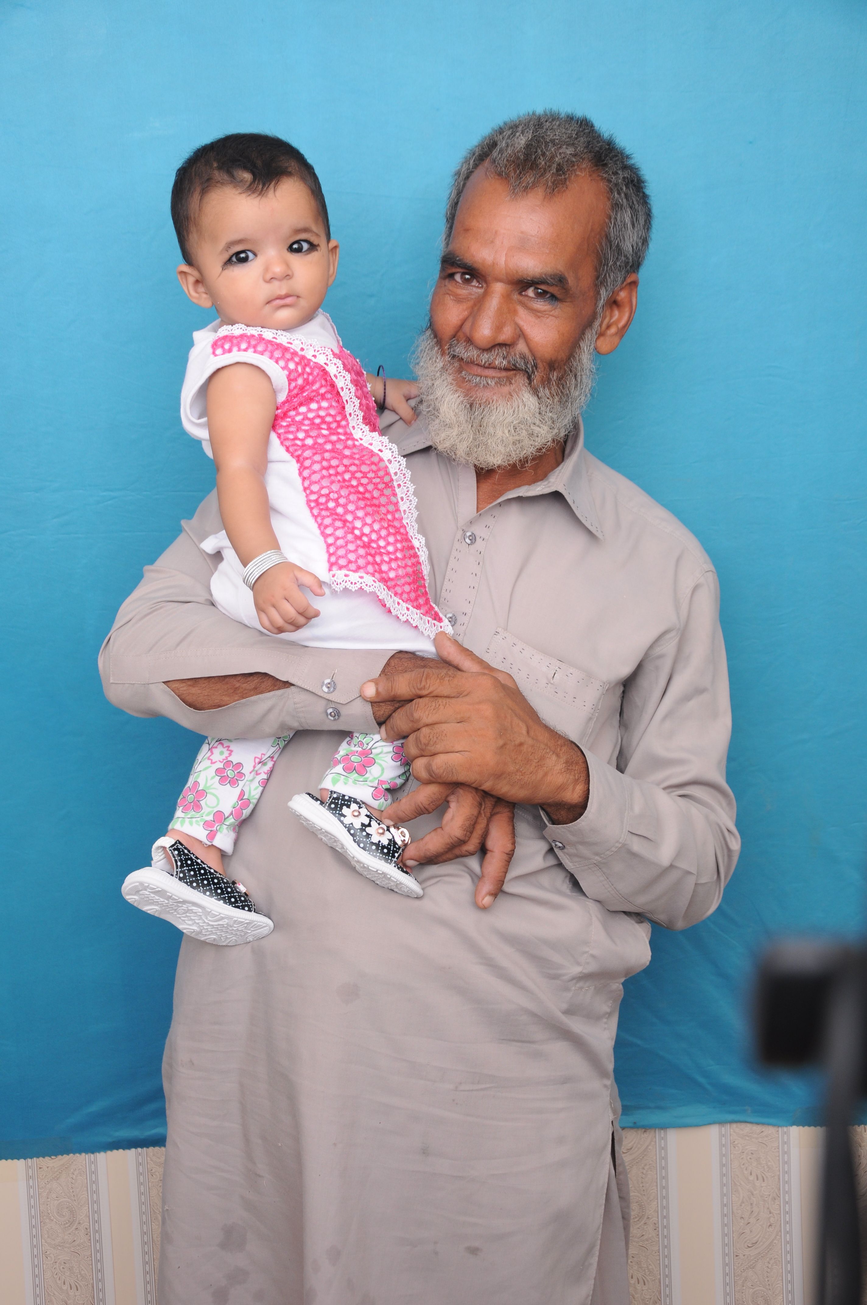 A grandfather holds his smiling granddaughter against a blue background.