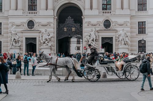 Free Tourists enjoy a horse-drawn carriage ride at Hofburg Palace in Vienna, Austria, showcasing historic architecture. Stock Photo
