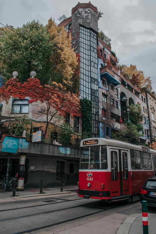 Free Red tram in front of the iconic Hundertwasserhaus in Vienna, showcasing eclectic architecture and autumn foliage. Stock Photo