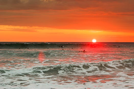 Experience a stunning Costa Rican sunset with surfers riding the waves against a vibrant orange sky.