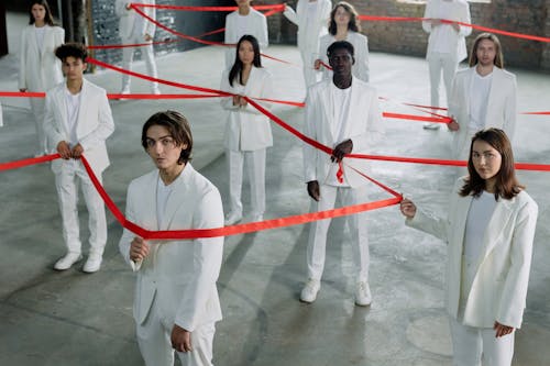 A High Angle Shot of People in White Clothes Holding a Red Ribbon