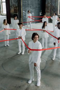 A diverse group of adults in white outfits holding red ribbons indoors, symbolizing connection and unity.