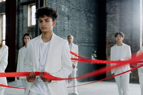 Man and Models in White Suits Holding Red Ribbon