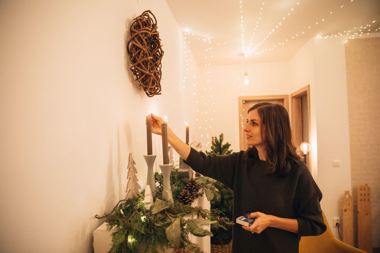 a woman lights candles in a cozy warmly decorated room during the fest