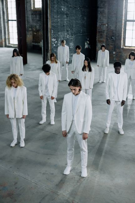 A diverse group of people dressed in white suits standing in an industrial setting.