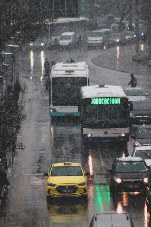 Free A busy city street in rainy weather featuring buses, cars, and reflections on wet asphalt. Stock Photo
