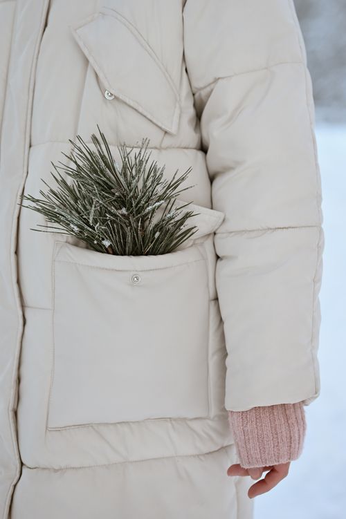 Free A white winter coat with a conifer twig peeking out of the front pocket, evoking a cozy winter feel. Stock Photo