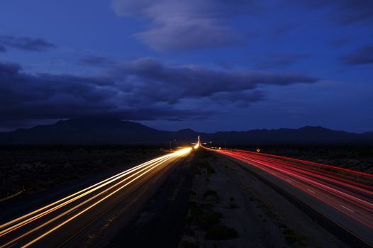A long exposure of a highway at night showcasing dynamic light trails under a cloudy sky.