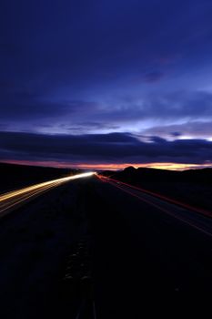 Captivating long exposure of a highway at sunset, showcasing vibrant light trails and a dramatic sky.