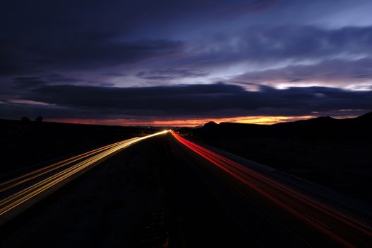 Long exposure photo of a highway at night with vibrant light trails and dramatic clouds.