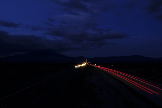 A dark aerial scene of a highway at night with illuminated light trails under a cloudy sky.