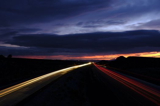 A captivating long exposure shot of highway traffic lights against a stunning sunset sky.