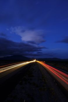 Dramatic long exposure of a highway at night, capturing vibrant car light trails under a deep blue sky.
