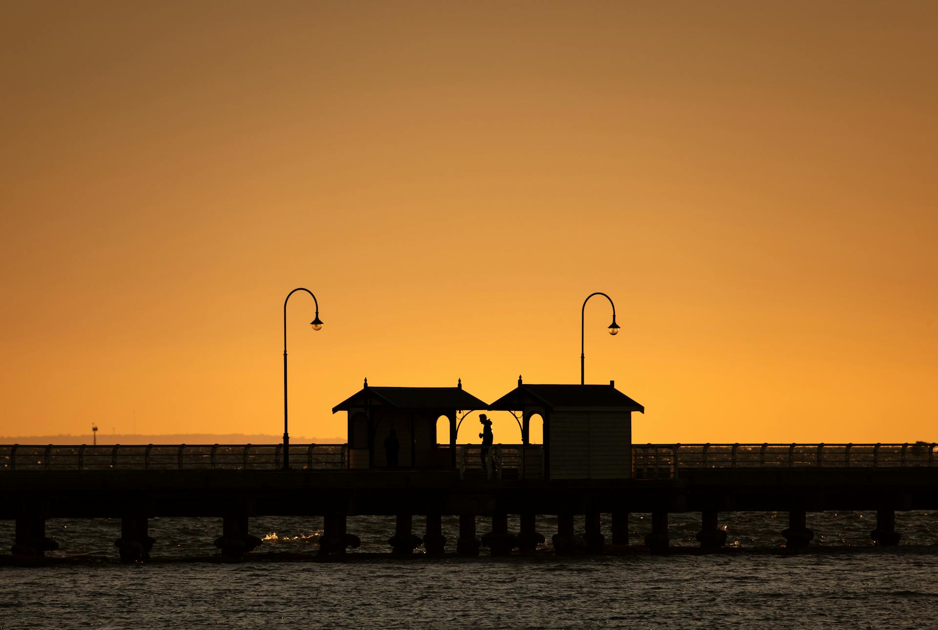 A silhouette view of Melbourne pier during a stunning sunset with golden hues.
