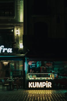 Illuminated Kumpir food stall on a quiet city street at night with cozy ambiance.