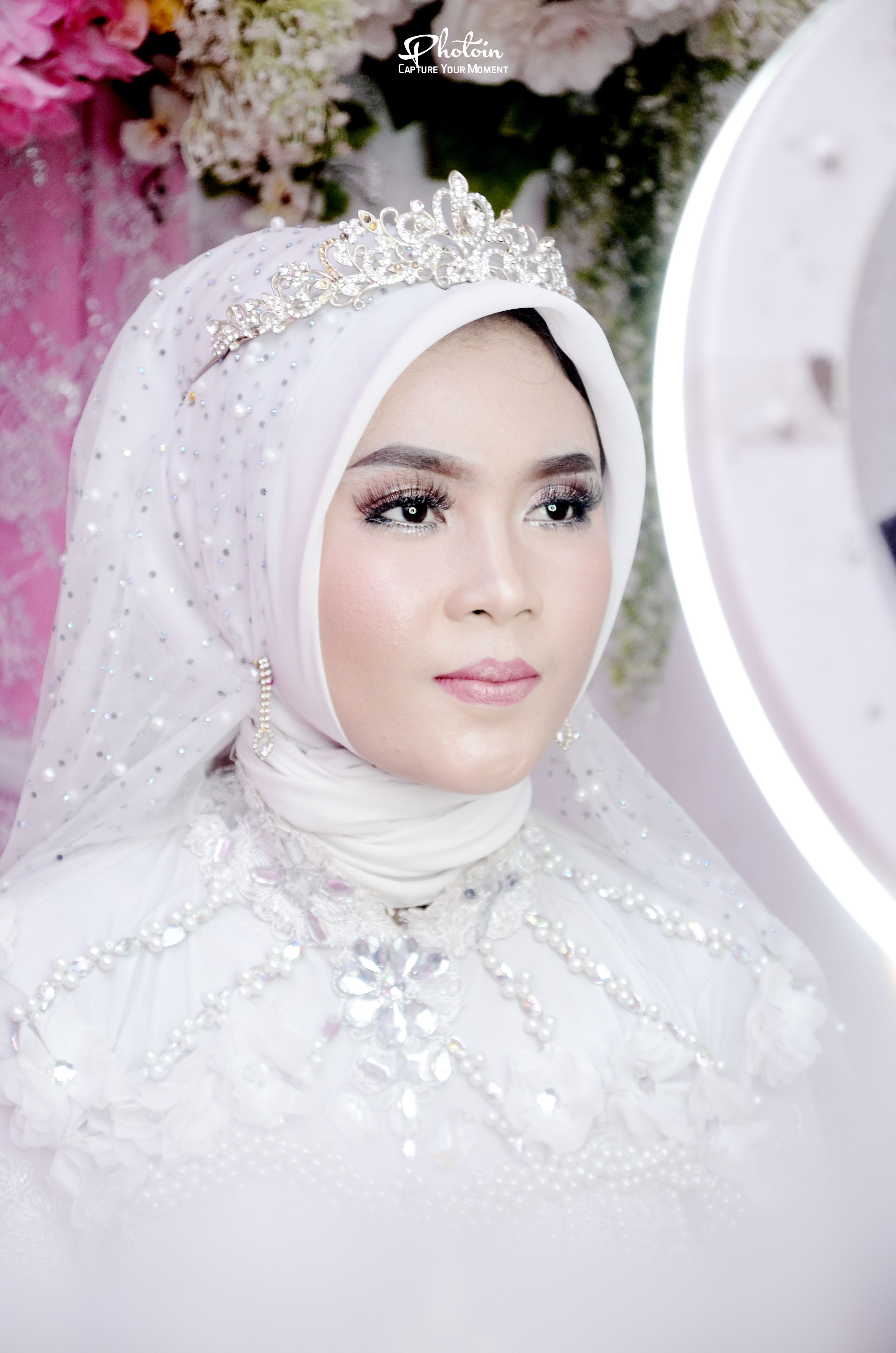 Close-up of a bride in a traditional embellished white hijab with a tiara, showcasing elegance and beauty.