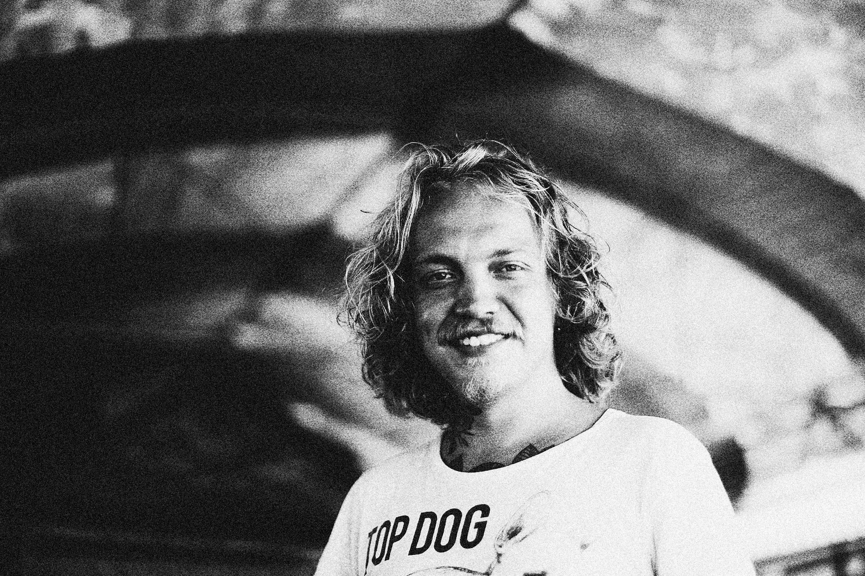 Monochrome portrait of a smiling man wearing a 'Top Dog' t-shirt, captured indoors.