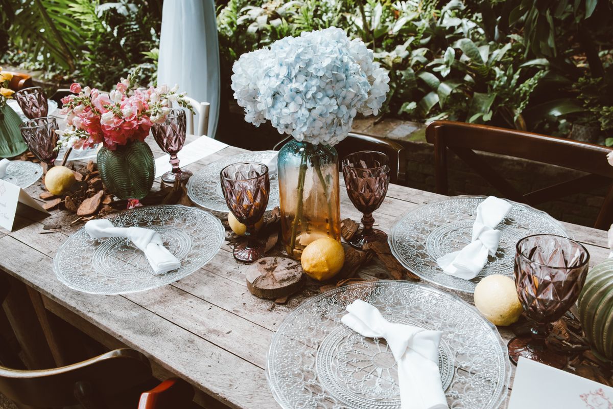 Charming rustic table setup with floral centerpiece and elegant glassware outdoors. Stock Photo.