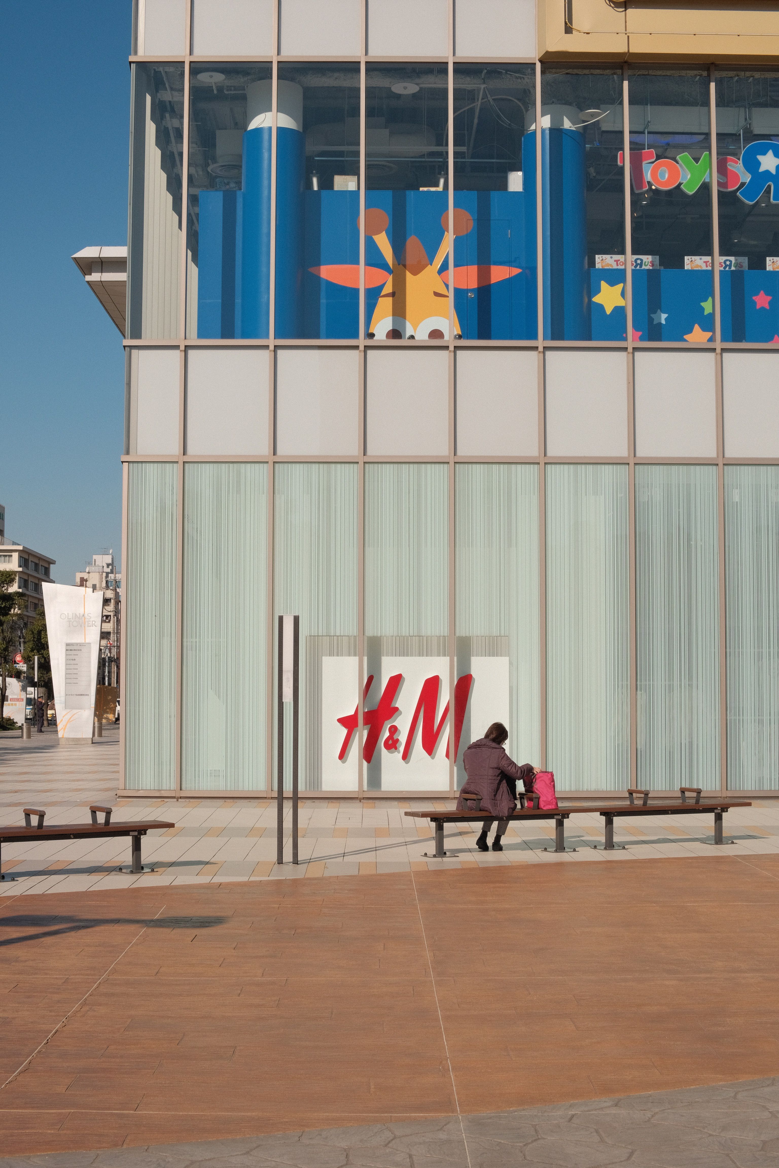 A person sitting on a bench outside an H&M store on a sunny day.