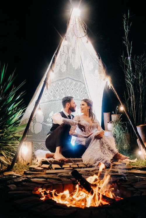 Free A loving couple embracing by a campfire beneath a lit teepee tent at night. Stock Photo