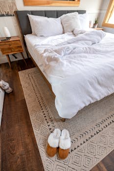 Inviting bedroom interior featuring plush white bedding, rustic decor, and comfy slippers for a relaxing ambiance.