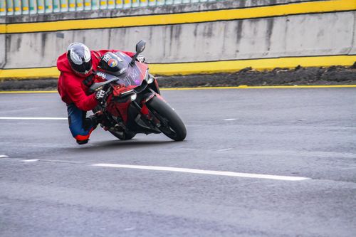 Free Motorcyclist in red hoodie skillfully leans into a sharp turn on an asphalt road. Stock Photo