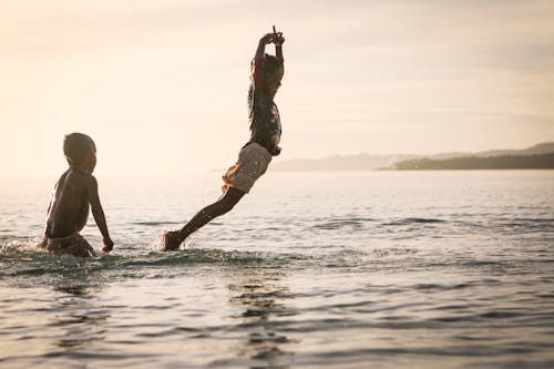 бесплатная Мальчик плывет над водой рядом с мальчиком, стоящим на боку Стоковое фото