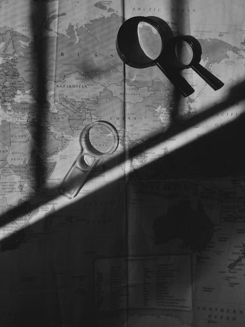 Grayscale Photo of Magnifying Glasses and a World Map
