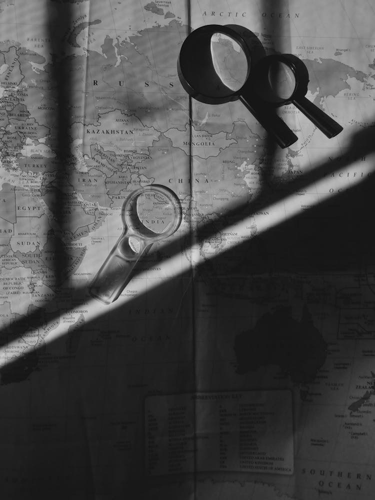 Grayscale Photo Of Magnifying Glasses And A World Map
