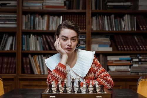 Free Woman sitting at a table in a library, playing chess with a serious expression. Stock Photo