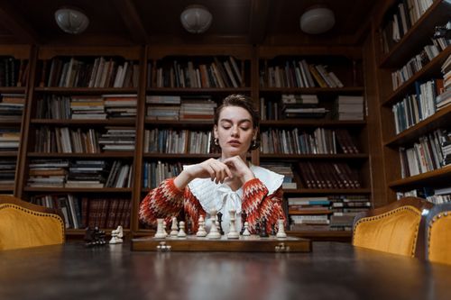 Free A woman deeply focused on playing chess in a cozy library setting. Stock Photo