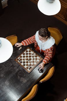 A woman intensely focused on a chess game, viewed from above, wearing a stylish red sweater.