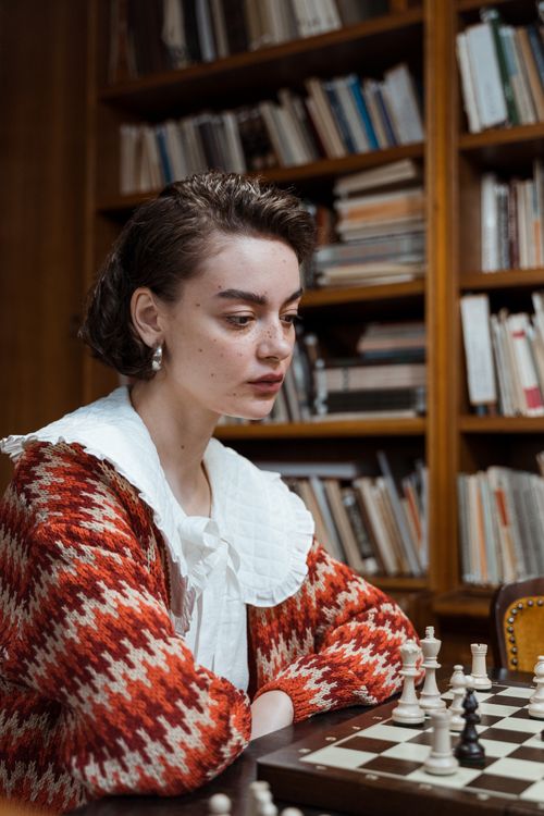 Free Woman deep in thought playing chess in a cozy library setting. Stock Photo