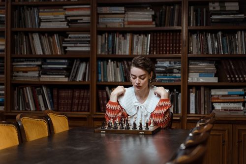 Free A woman deeply focused on playing chess in a cozy library setting. Stock Photo