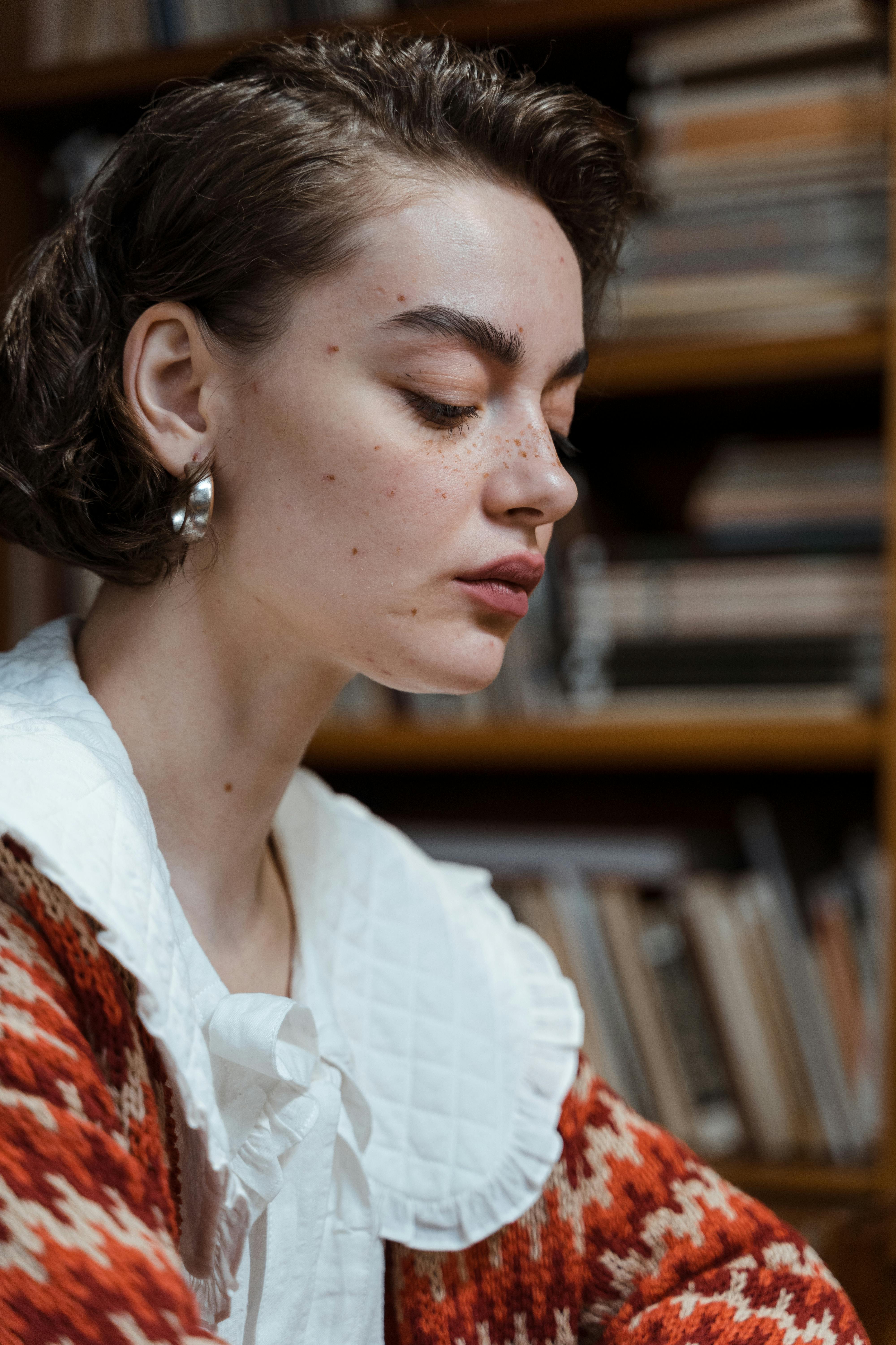 Elegant young woman in profile against a backdrop of books in a library.
