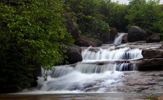 A tranquil waterfall cascading over rocks amidst lush greenery, captured in a serene natural setting.