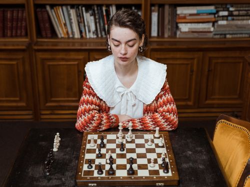 Free A woman in a library focusing intensely on a chess game, embodying strategy and concentration. Stock Photo