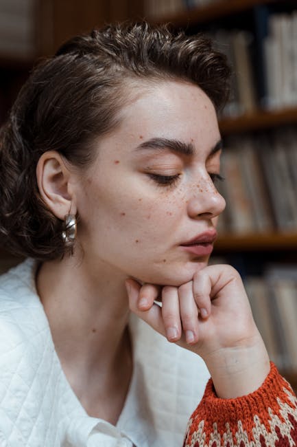 Side profile of a woman in a library, wearing a sweater and earrings, deep in thought.