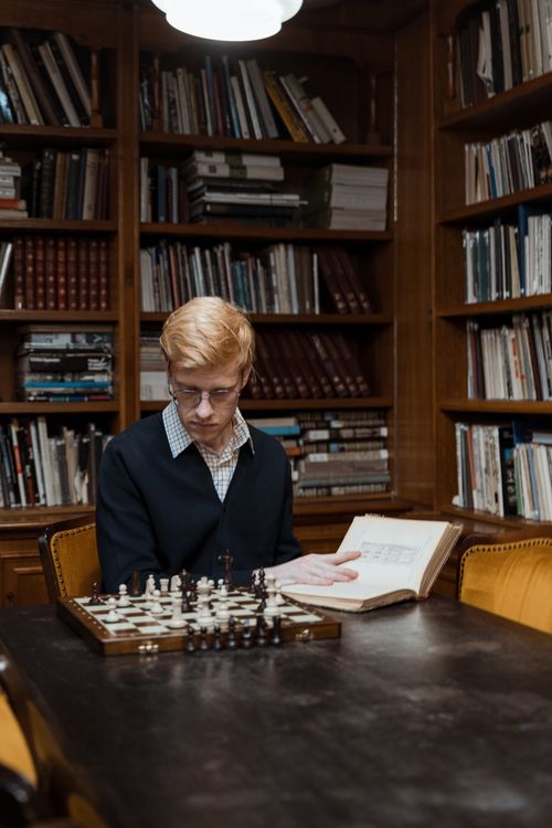 Free Man sits in a library reading while contemplating a chess game. Stock Photo