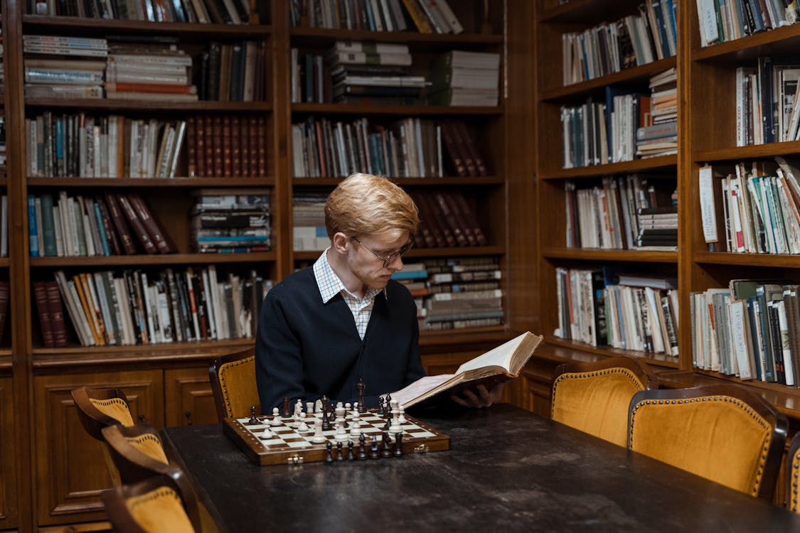 A Man Sitting Inside the Library while Reading a Book