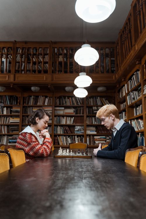 Free Two individuals deep in thought, playing chess in a cozy library setting. Stock Photo