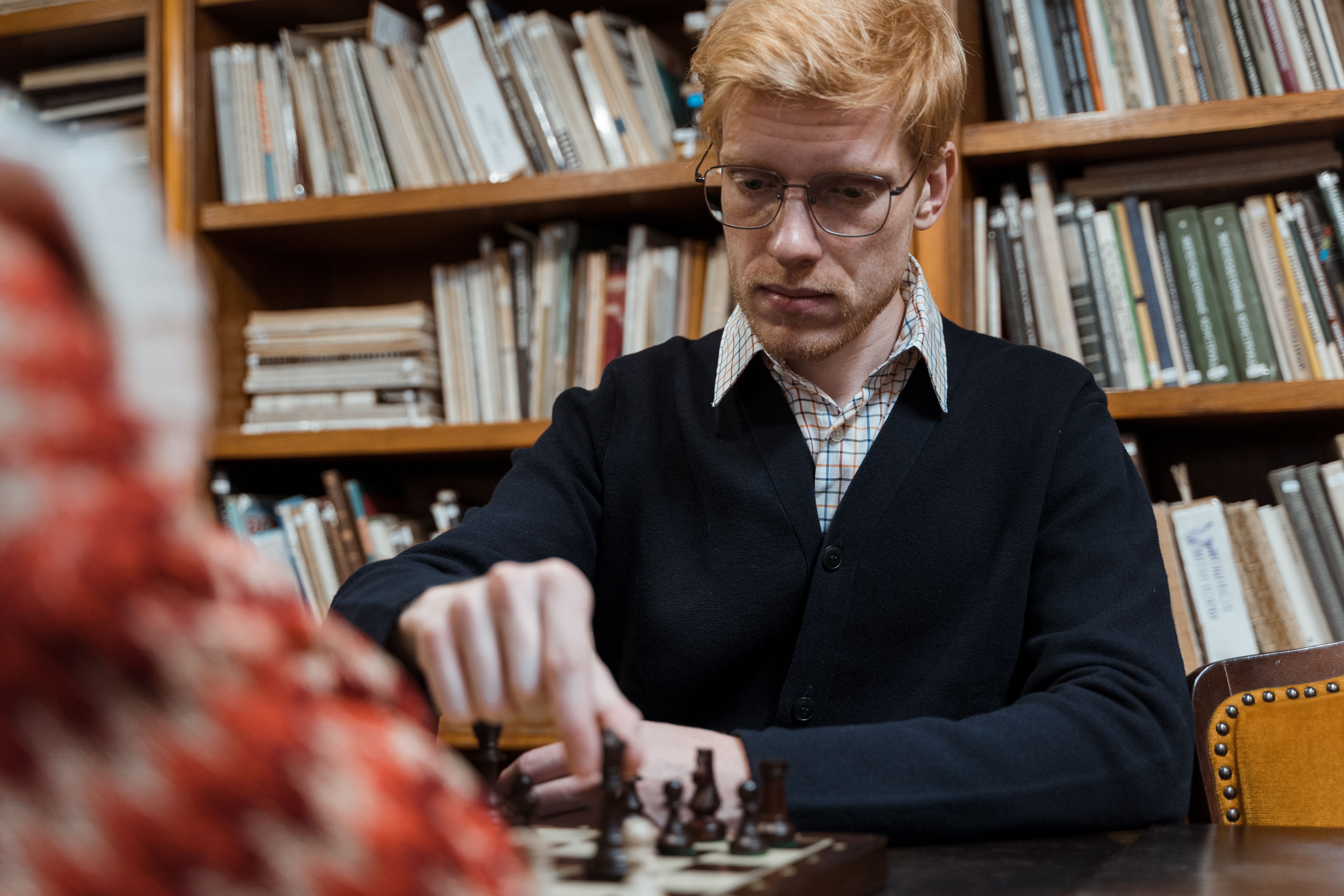 Man playing chess, deeply focused, in a cozy library environment.